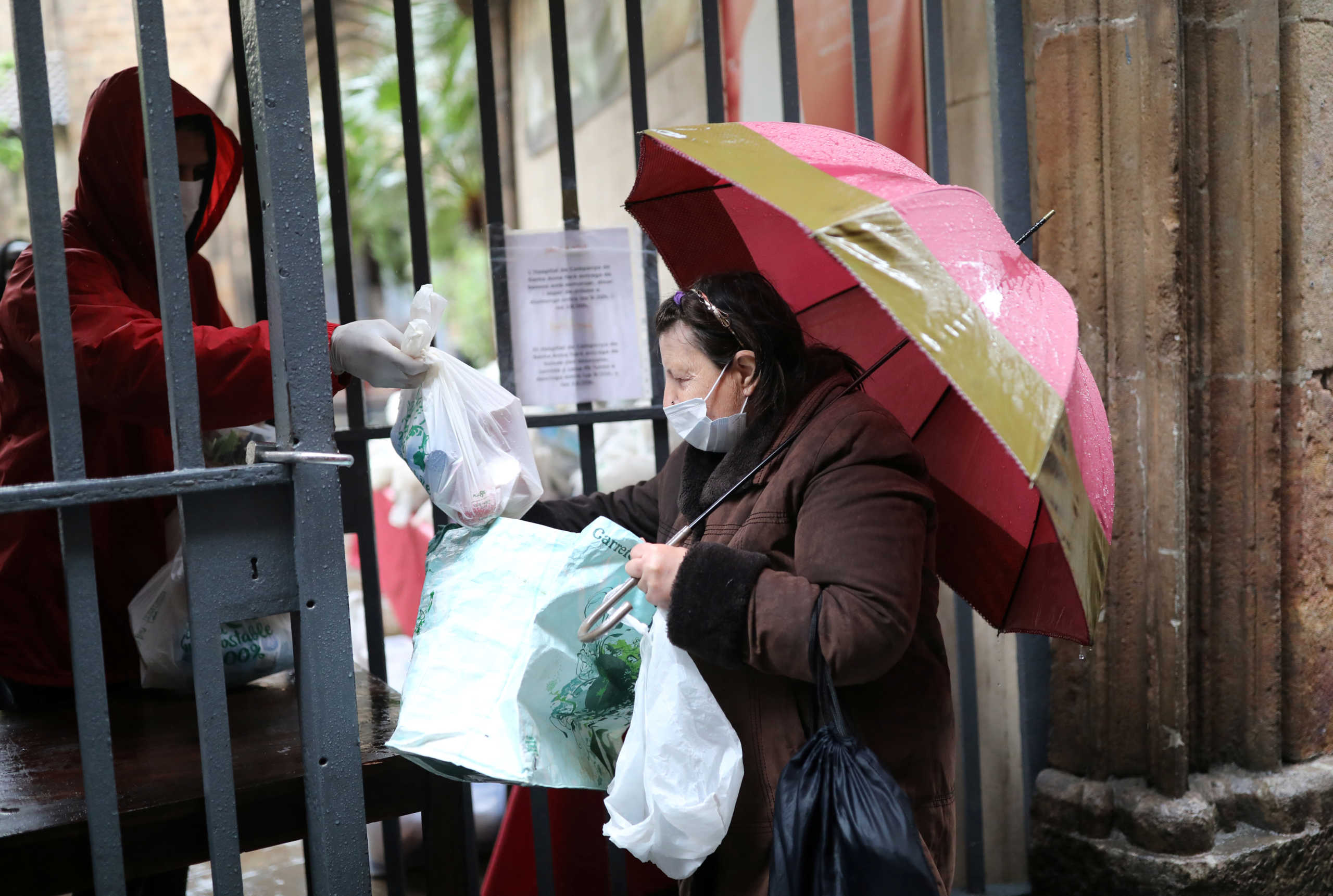 A volunteer gives free food packages for a woman amid economic hardship outside parish church of Santa Anna, amid the spread of the coronavirus disease (COVID-19), in Barcelona, Spain, April 21, 2020. REUTERS