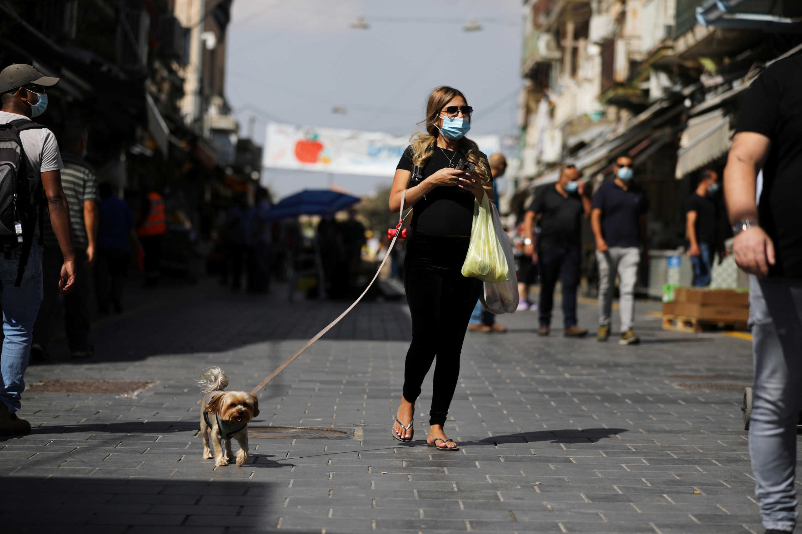 A woman wearing a protective face mask walks with a dog at a market amid Israel's second-wave coronavirus disease (COVID-19) lockdown, in Jerusalem October 5, 2020. REUTERS