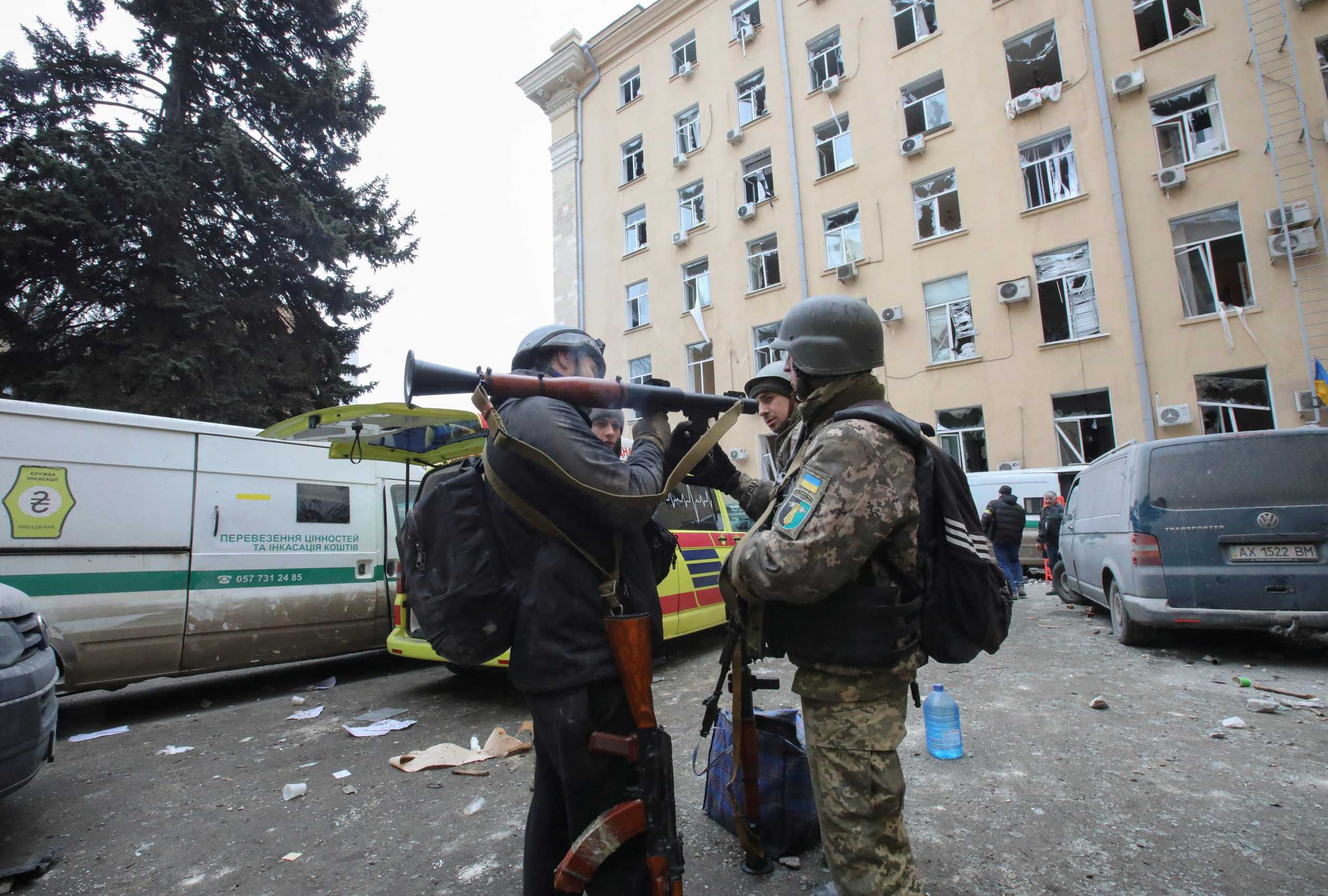 People hold weapons outside the regional administration building, which city officials said was hit by a missile attack, in central Kharkiv, Ukraine, March 1, 2022. REUTERS