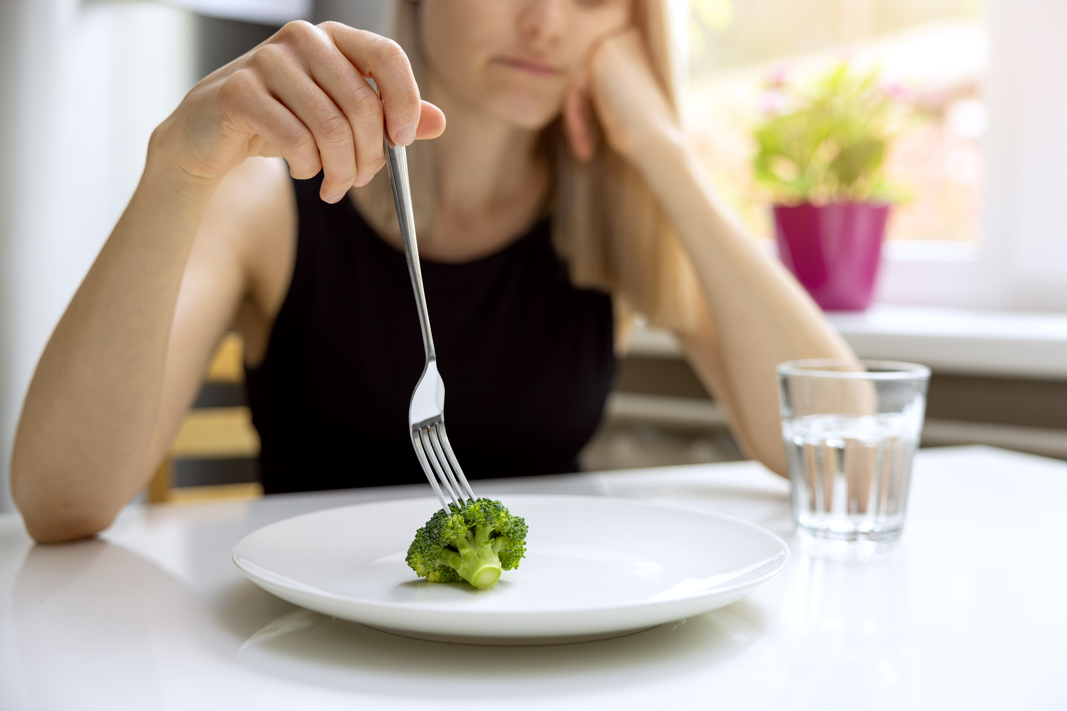 dieting problems, eating disorder - unhappy woman looking at small broccoli portion on the plate