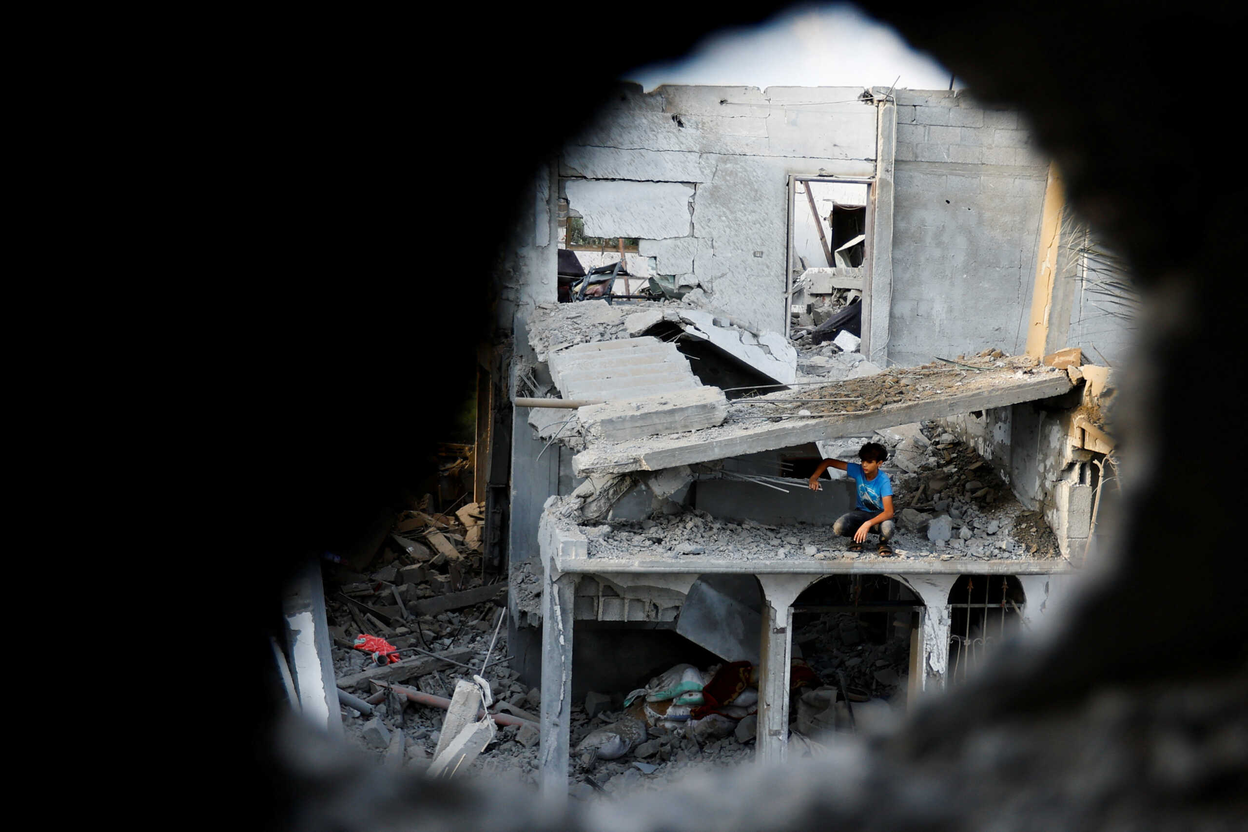 A Palestinian boy sits on a damaged house as seen through rubble, following Israeli strikes, in Khan Younis in the southern Gaza Strip October 11, 2023. REUTERS