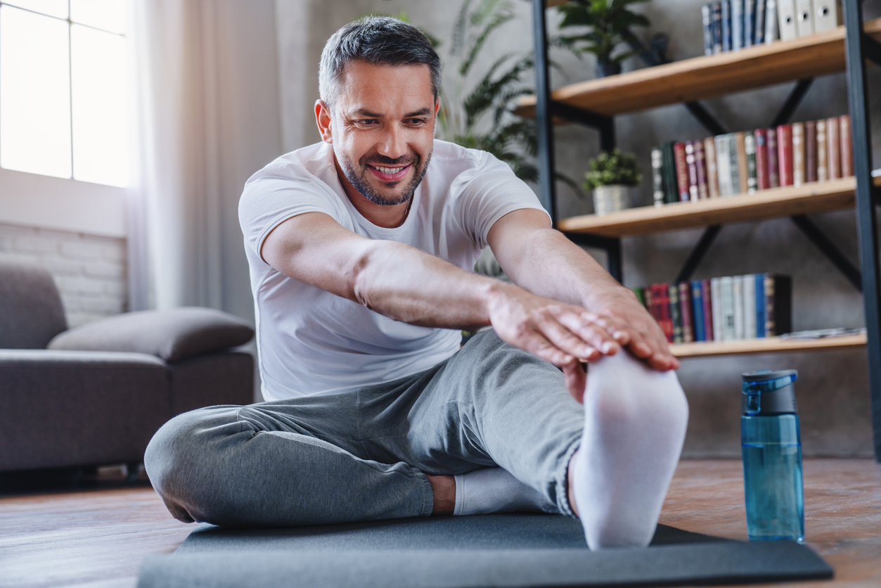 Handsome man doing hamstring stretch exercise at home.