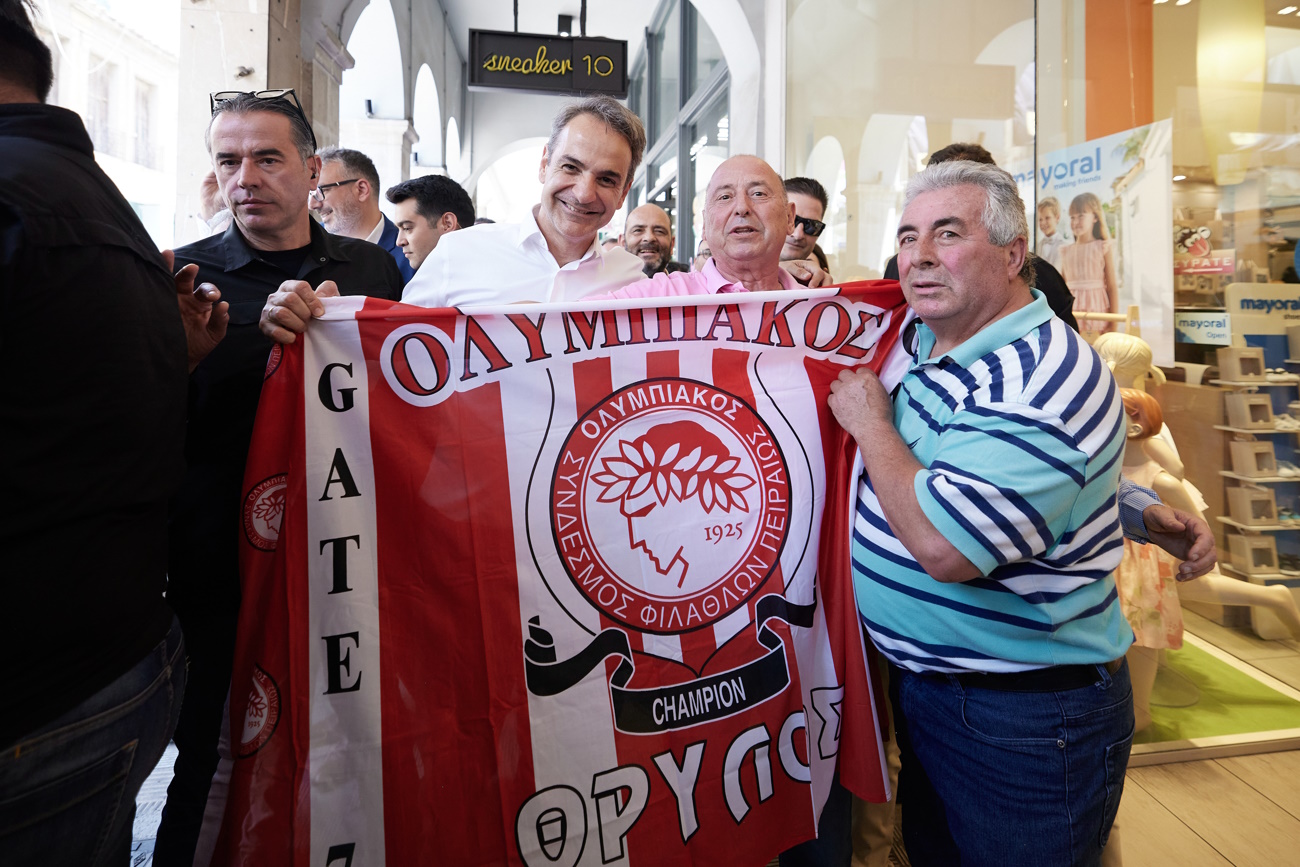 Ο Κυριάκος Μητσοτάκης κρατάει χαμογελαστός τη σημαία του Ολυμπιακού