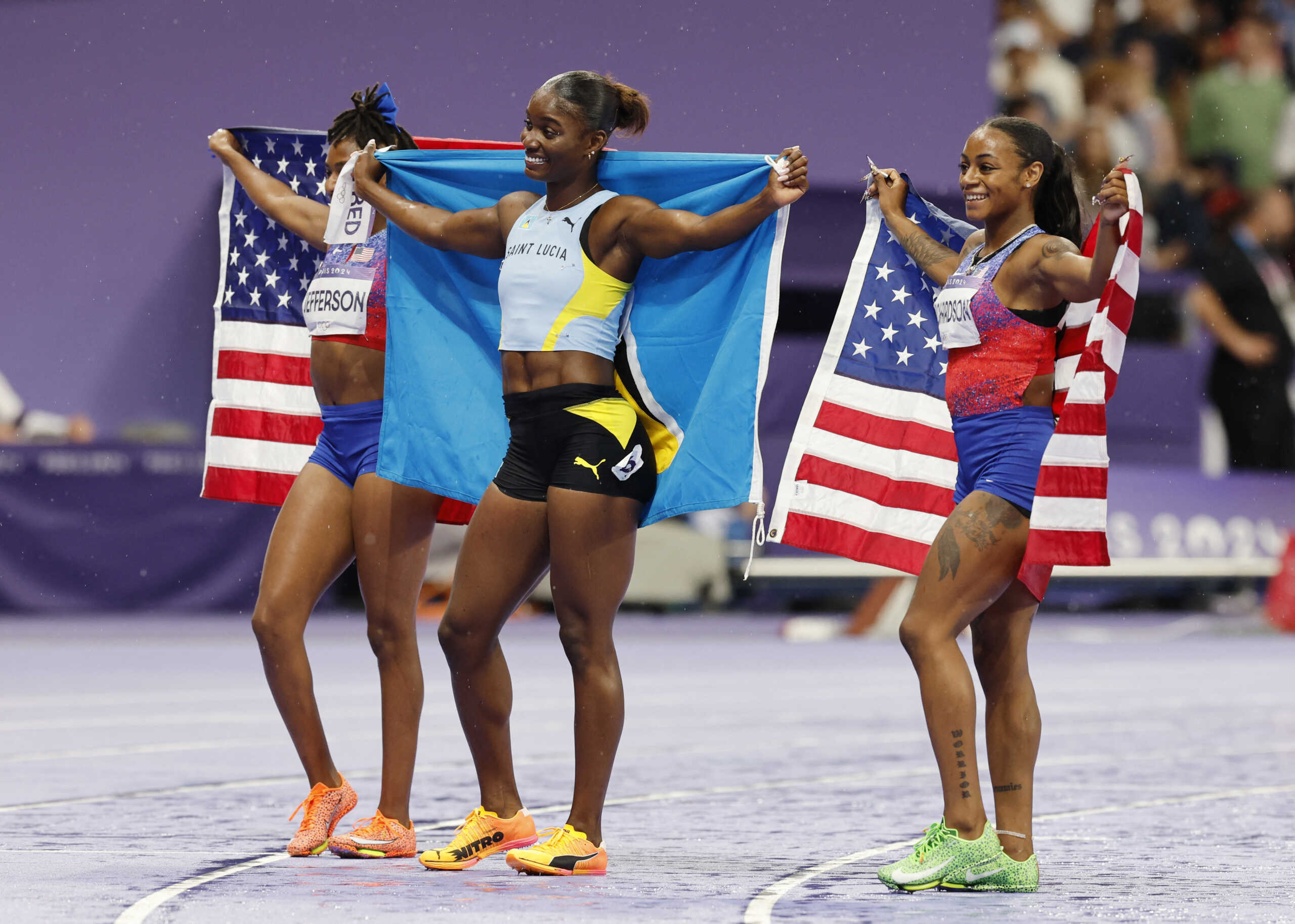 Paris 2024 Olympics - Athletics - Women's 100m Final - Stade de France, Saint-Denis, France - August 03, 2024. Julien Alfred of Saint Lucia celebrates with her national flag after winning gold in the final with silver medallist Sha'Carri Richardson of United States and bronze medallist Melissa Jefferson of United States REUTERS