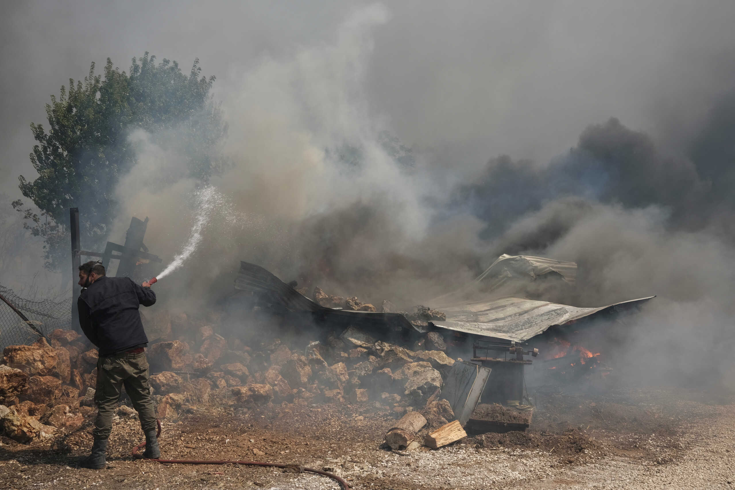 A man tries to extinguish a fire burning a house as a wildfire burns in Nea Penteli, Greece, August 12, 2024. REUTERS