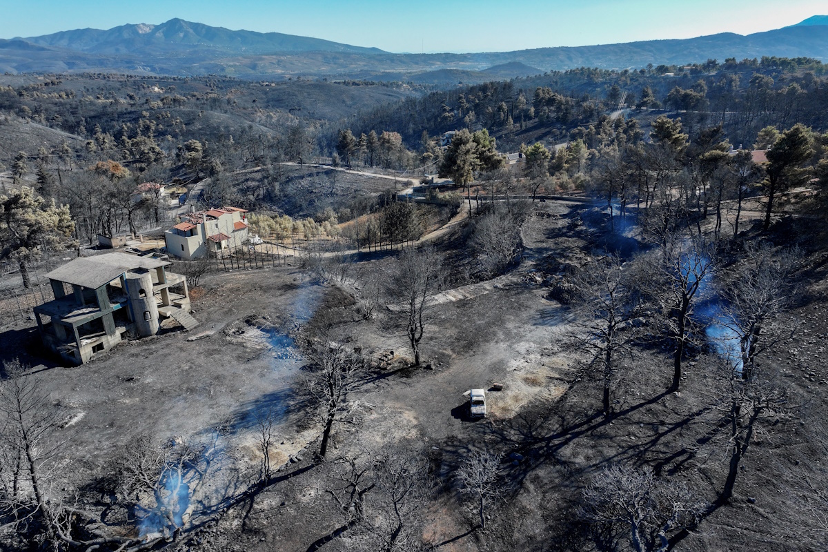 A drone view shows destroyed houses and a destroyed car in a charred forest area following a wildfire, in the village of Varnavas, Greece, August 13, 2024. REUTERS