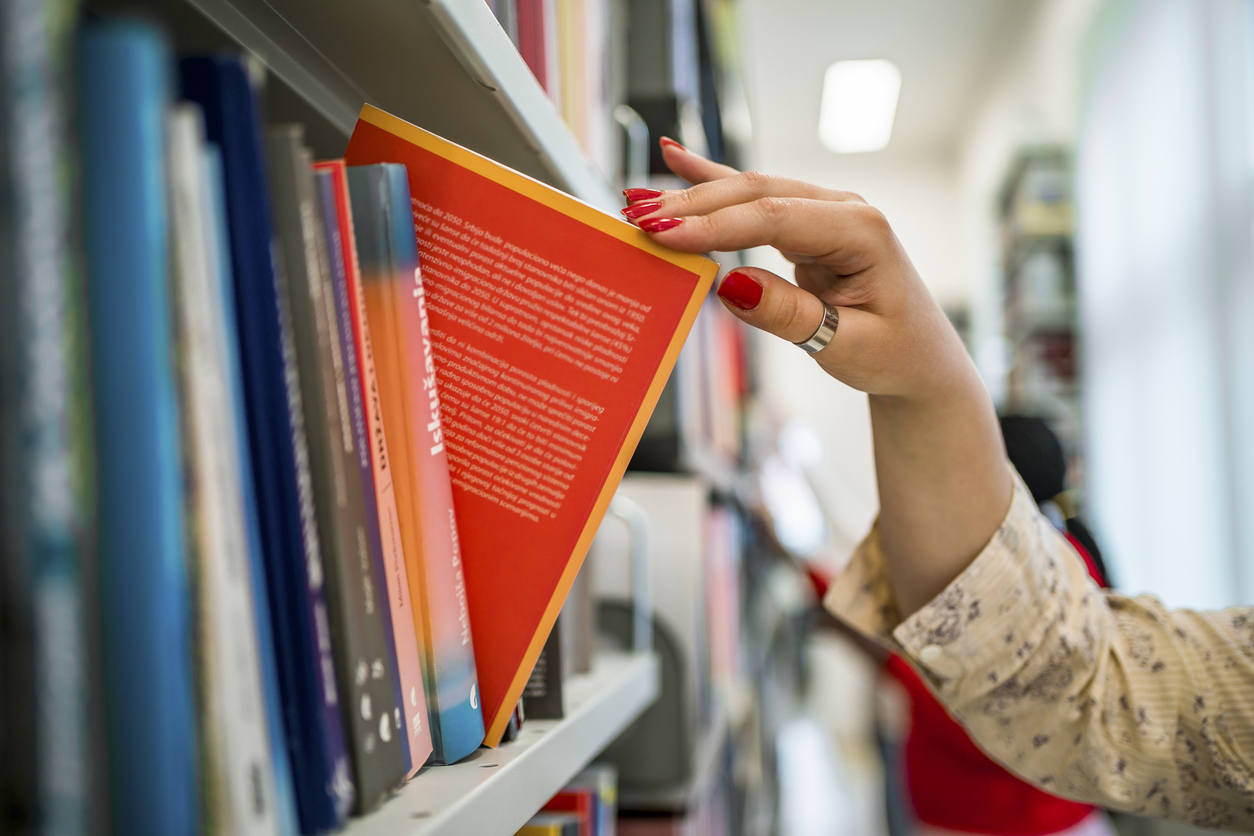 Woman's hand picking a book from a library bookshelf