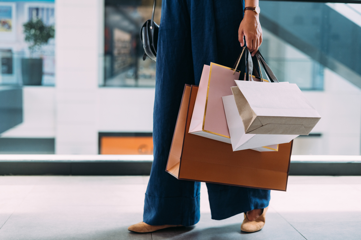 An unrecognizable Caucasian female standing at the shopping mall with paper bags.