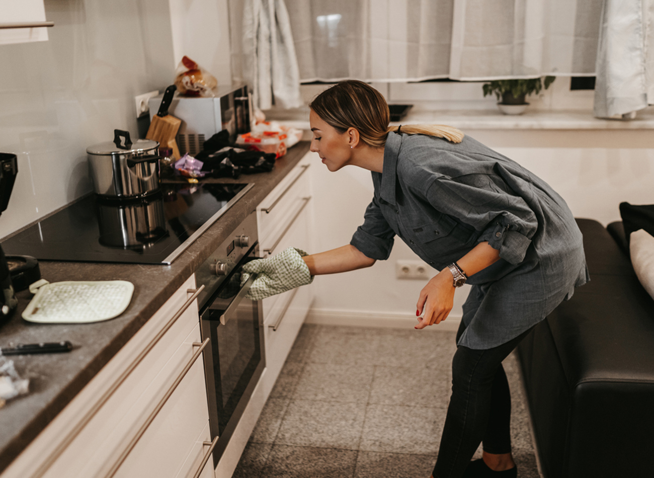 Young woman in kitchen opening oven to check meal