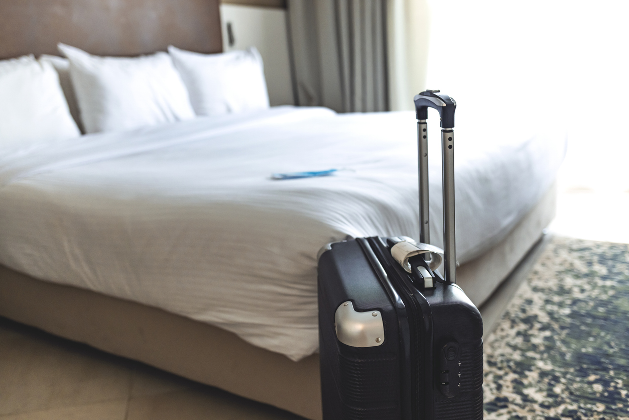 Close up of black luggage and surgical mask. Hotel room bed background, copy space for text, Traveling in new normal lifestyle concept. Stay safe while travel during Covid 19 pandemic concept.