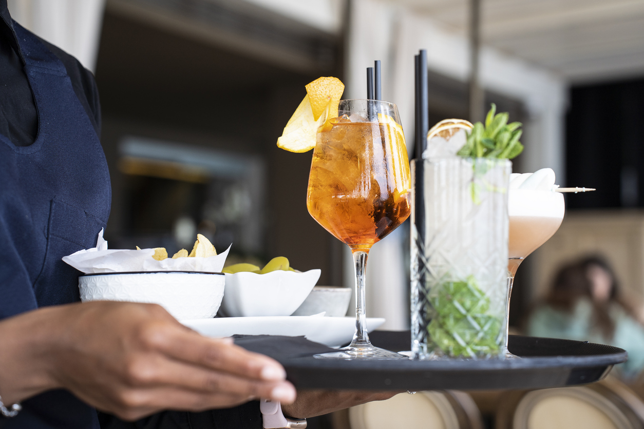 Closeup of tray with cocktails and appetizers - Spritz and mojito served by an African waitress in the restaurant bar