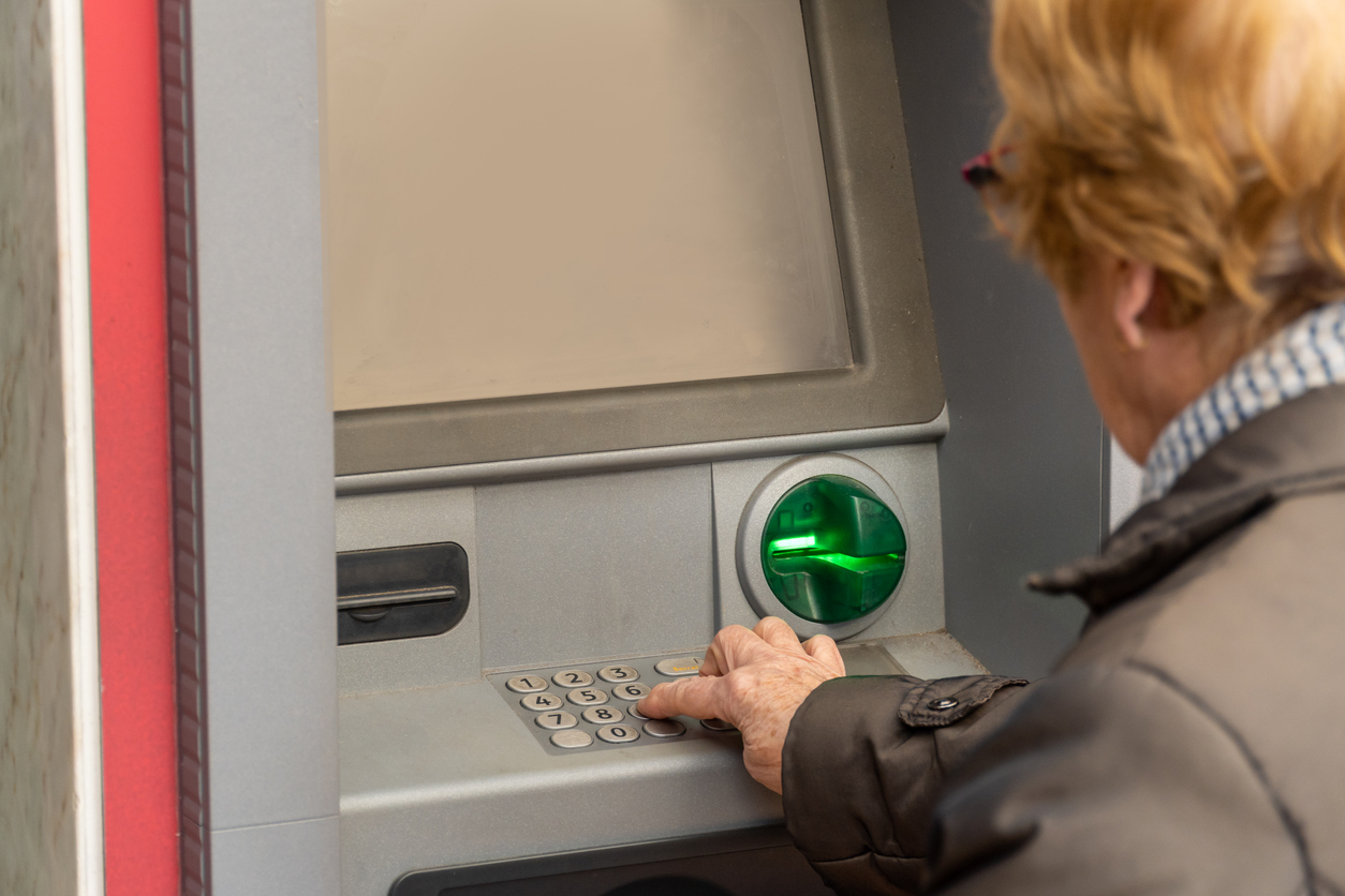 Close up, an elderly woman uses an ATM