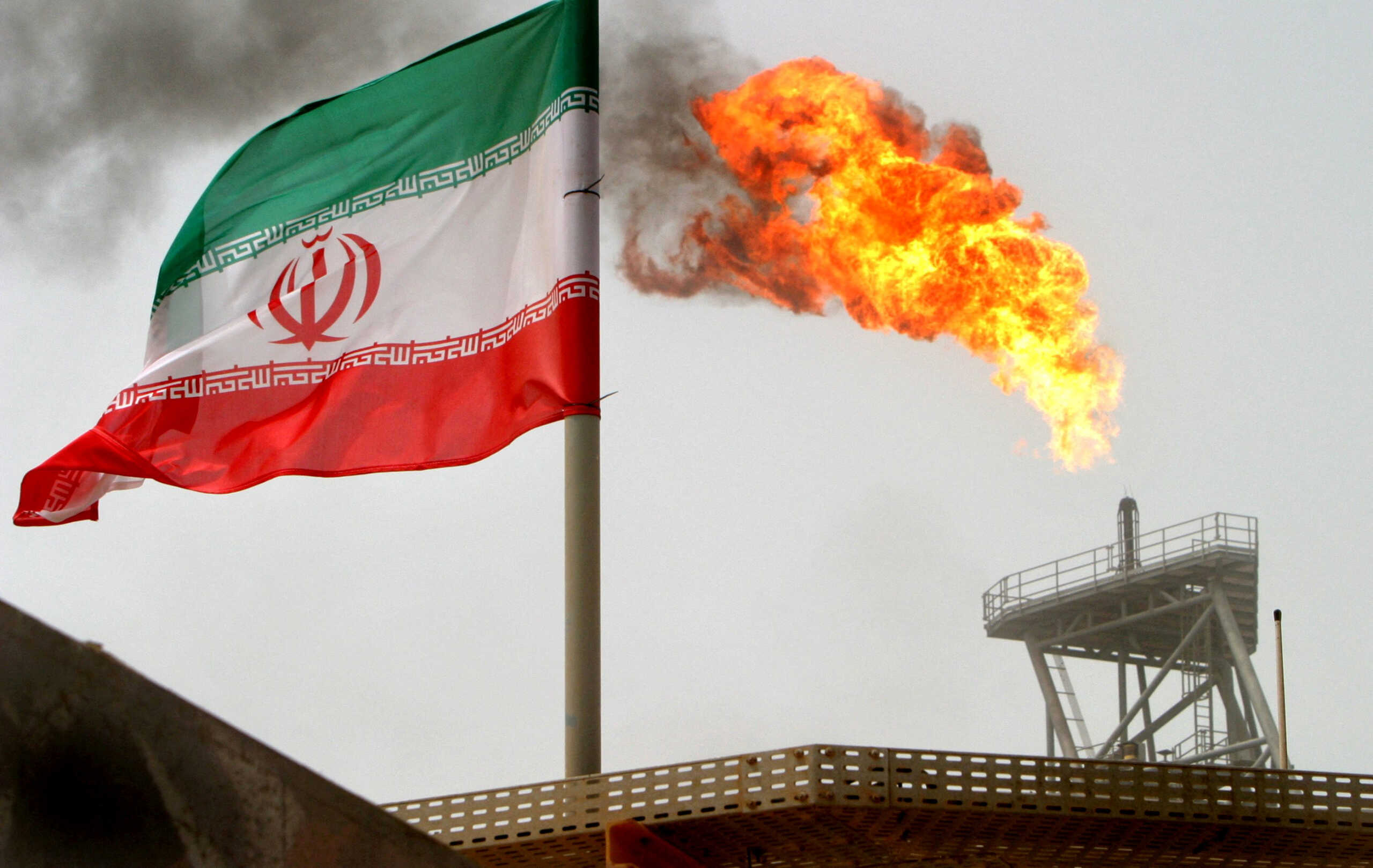 FILE PHOTO: A gas flare on an oil production platform is seen alongside an Iranian flag in the Gulf July 25, 2005. REUTERS