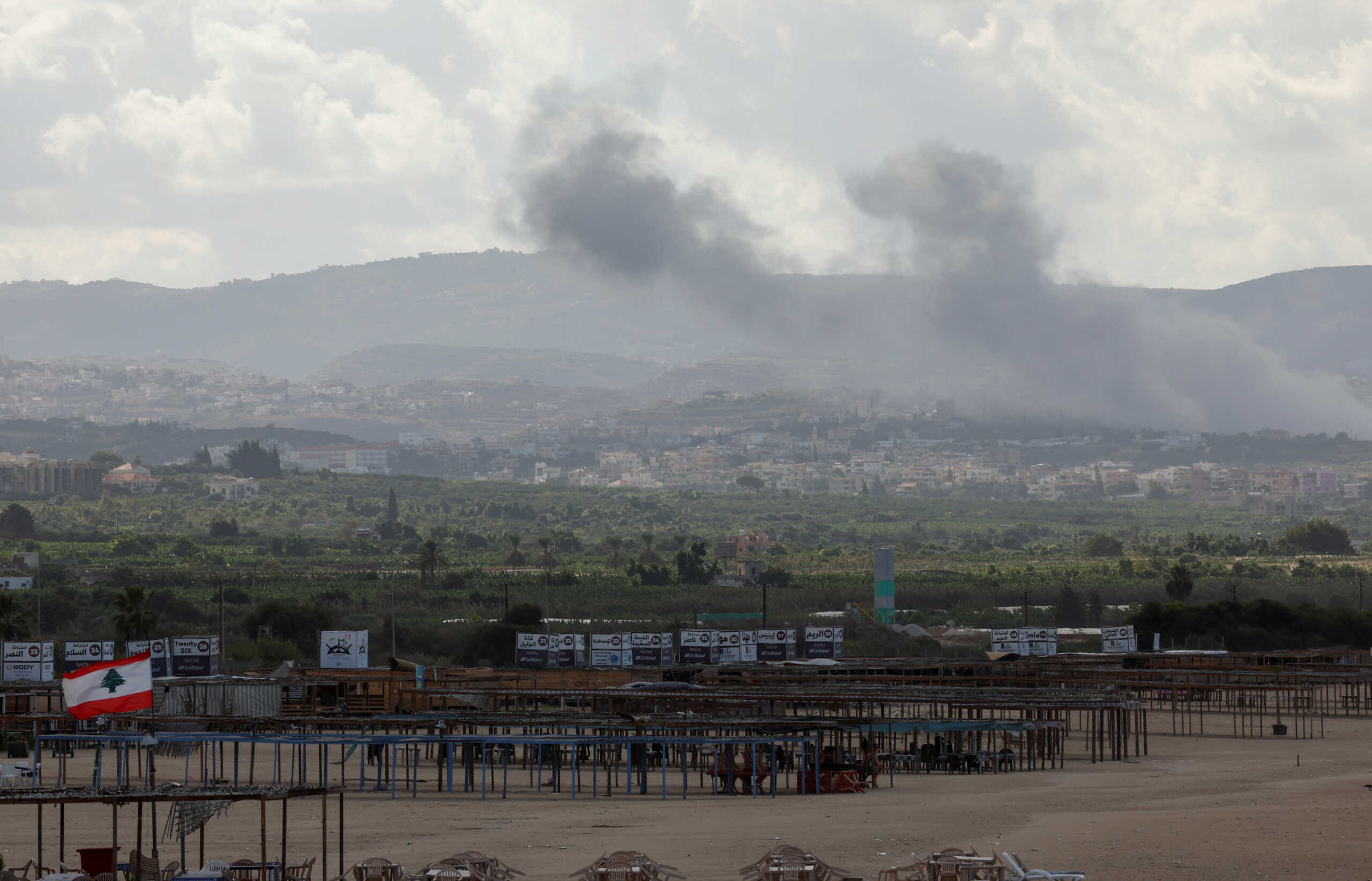 A Lebanese flag flutters in the wind as smoke billows, amid the ongoing hostilities between Hezbollah and Israeli forces, as seen from Tyre, southern Lebanon October 2, 2024. REUTERS