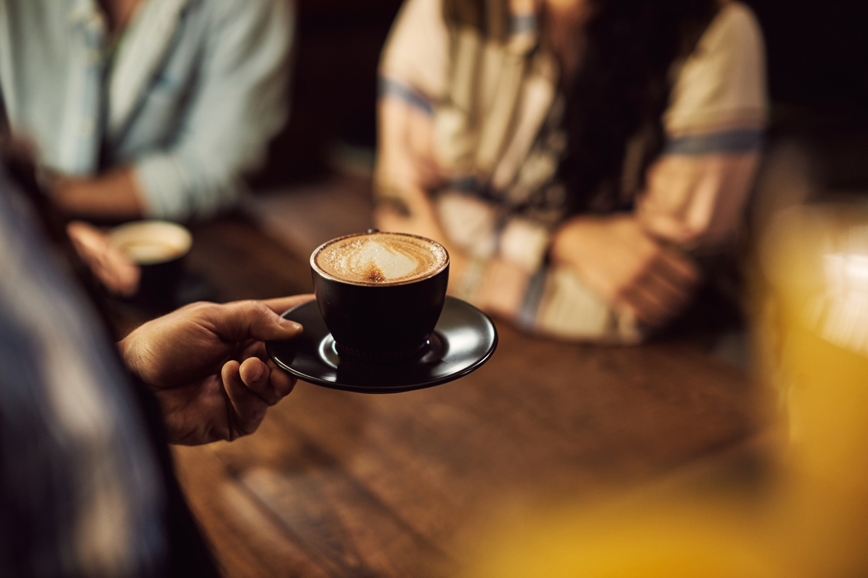 Close-up of waiter serving coffee to customers while working in a cafe.