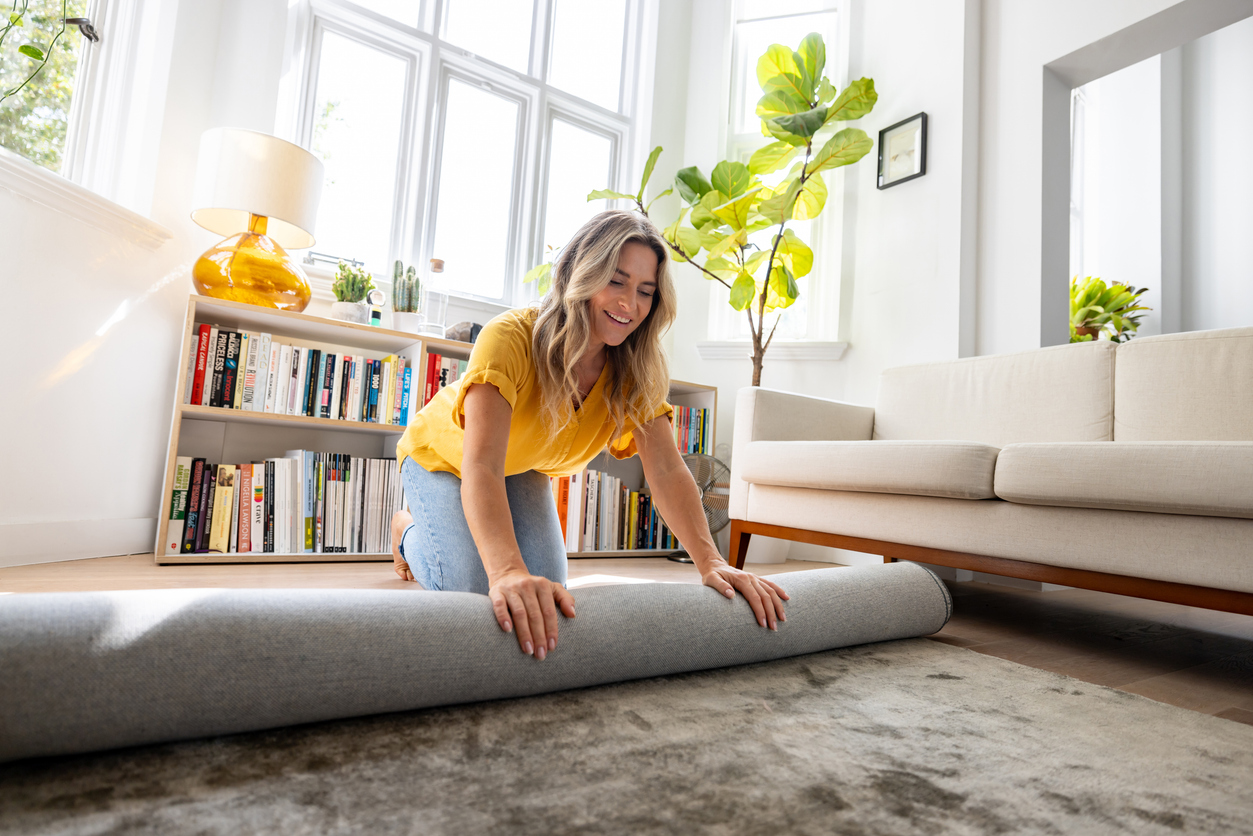 Happy Caucasian woman moving house and unrolling a carpet while unpacking - domestic life concepts