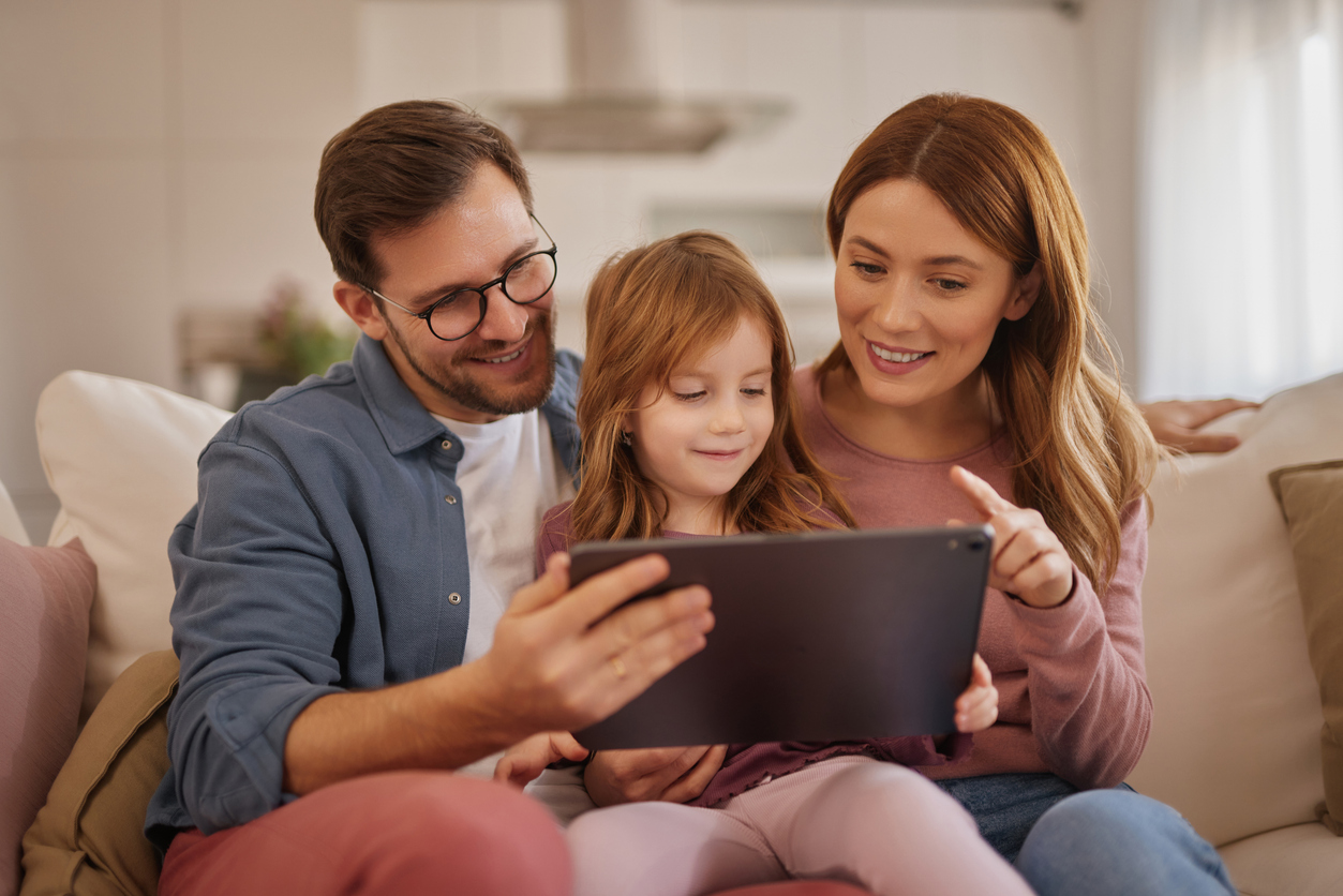 Curious little girl using the tablet with her parents in the living room