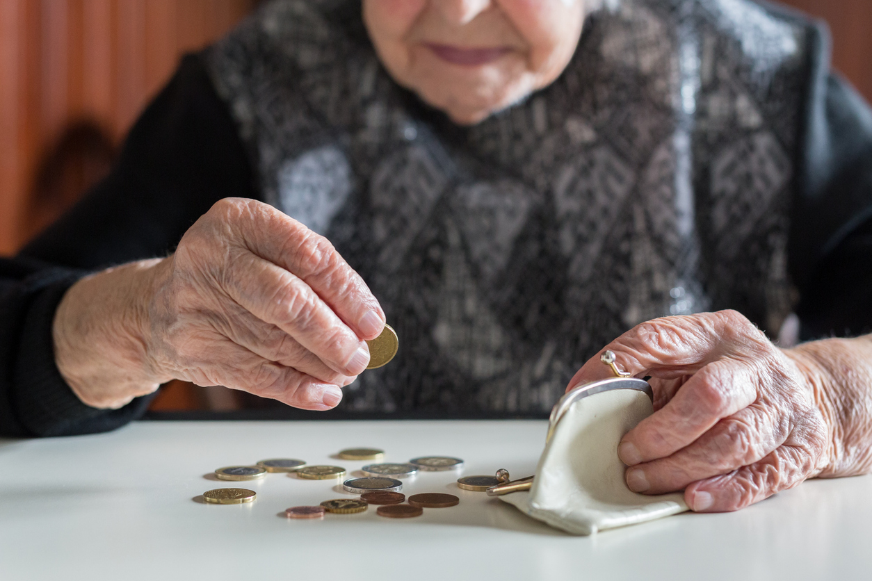 Elderly 95 years old woman sitting miserably at the table at home and counting remaining coins from the pension in her wallet after paying the bills.