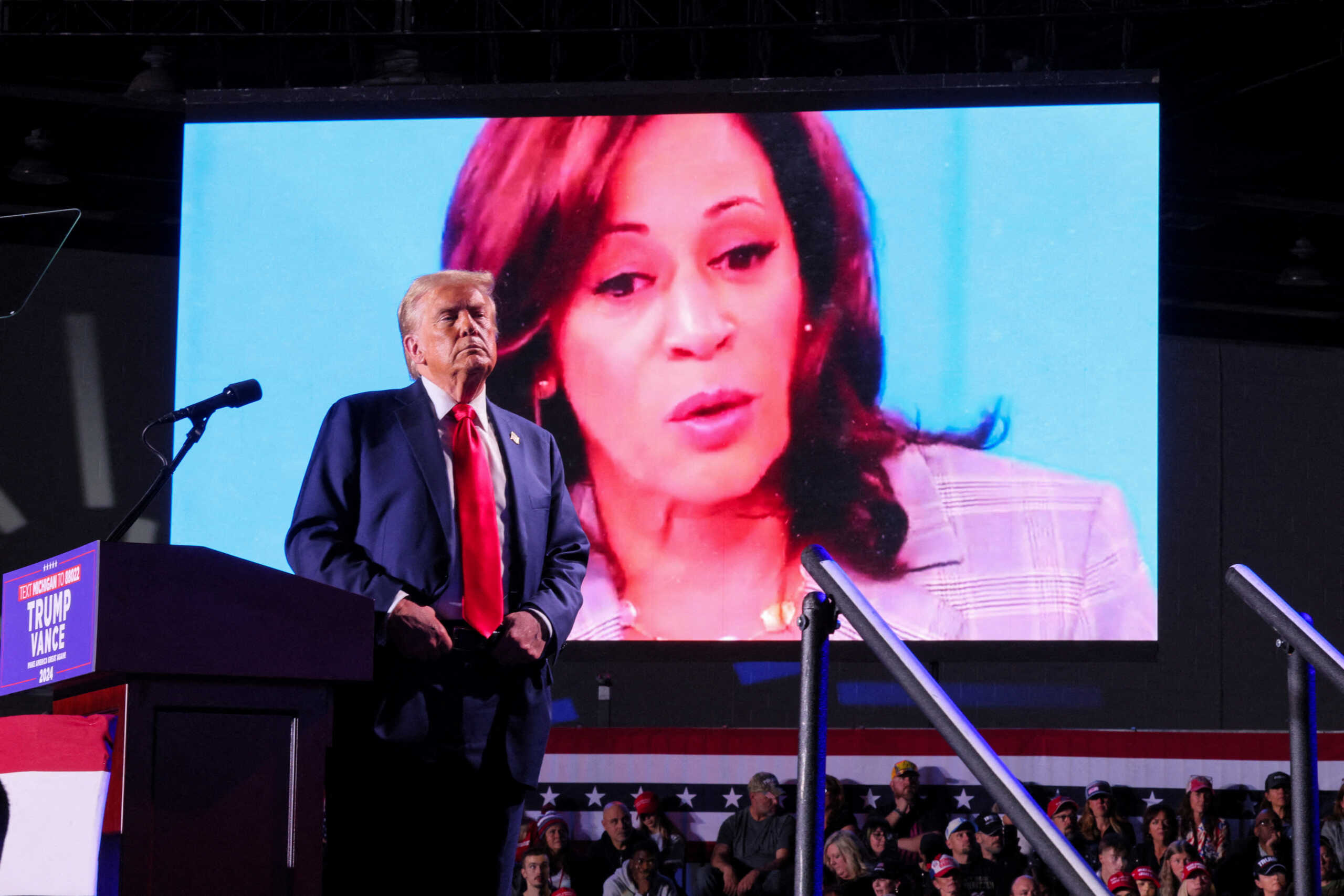 FILE PHOTO: Republican presidential nominee and former U.S. President Donald Trump looks on as Democratic presidential nominee and U.S. Vice President Kamala Harris' face appears as a video plays on a screen, during a rally at Huntington Place in Detroit, Michigan, U.S. October 18, 2024.  REUTERS