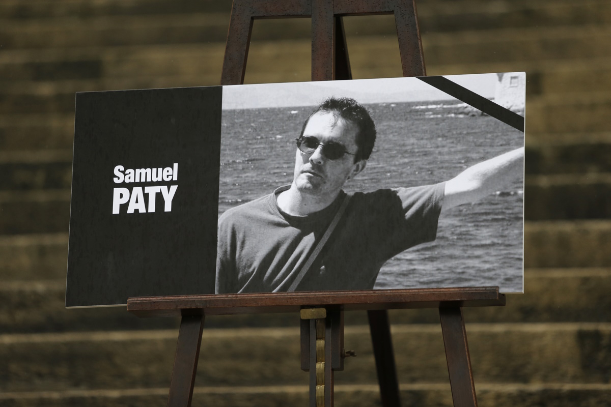 The portrait of slain teacher Samuel Paty with a black ribbon is displayed Tuesday, Oct.20, 2020 on the steps of the National Assembly in Paris. A memorial march will be held Tuesday evening near Paris in homage to the history teacher who was beheaded last week, while French police said 16 people remain in custody as part of the investigation into the attack. (AP Photo