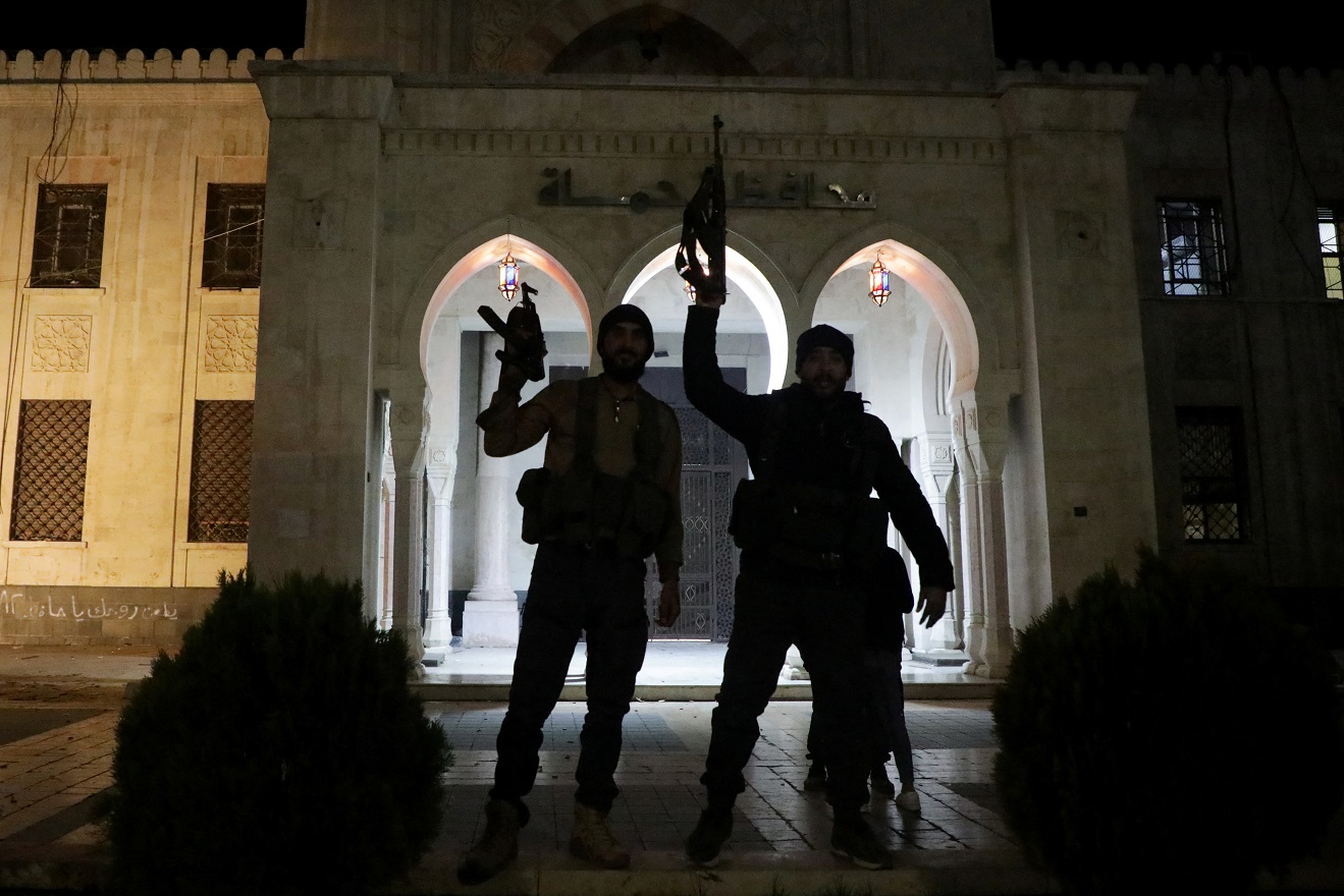 Rebel fighters hold weapons in front of Hama governor's building as they gather after Syrian rebels captured the city during their advance across northern Syria, in Hama, Syria December 5, 2024. REUTERS