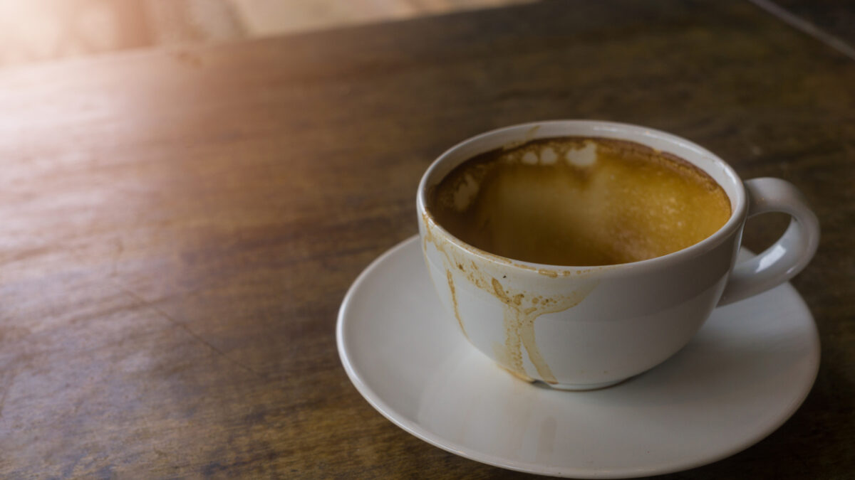 Coffee stains on a white coffee cup that placed on the brown wooden table in the morning, the sun shinning on a part of table