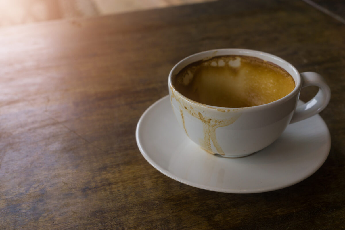 Coffee stains on a white coffee cup that placed on the brown wooden table in the morning, the sun shinning on a part of table