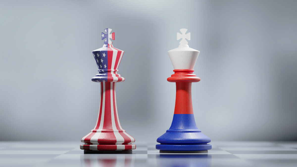 Two king chess pieces textured with American and Russian flags on black and white chessboard. Politics and checkmate concept. Horizontal composition with selective focus and copy space.