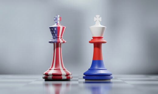 Two king chess pieces textured with American and Russian flags on black and white chessboard. Politics and checkmate concept. Horizontal composition with selective focus and copy space.