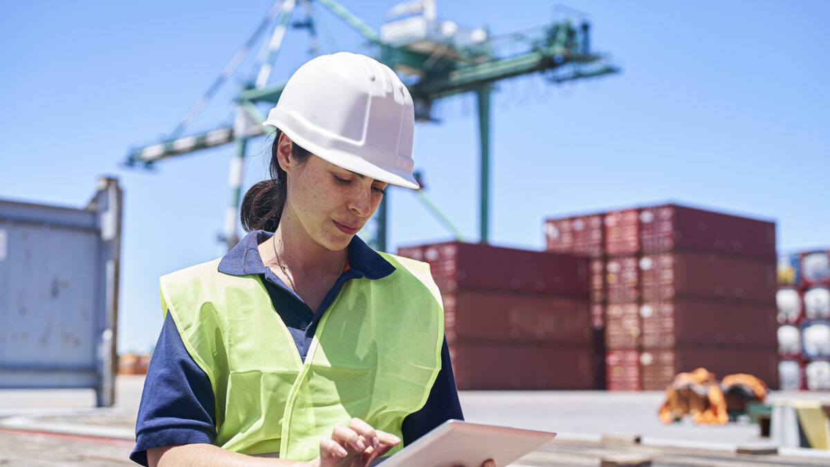 Female engineer sitting on ship dock while using digital tablet