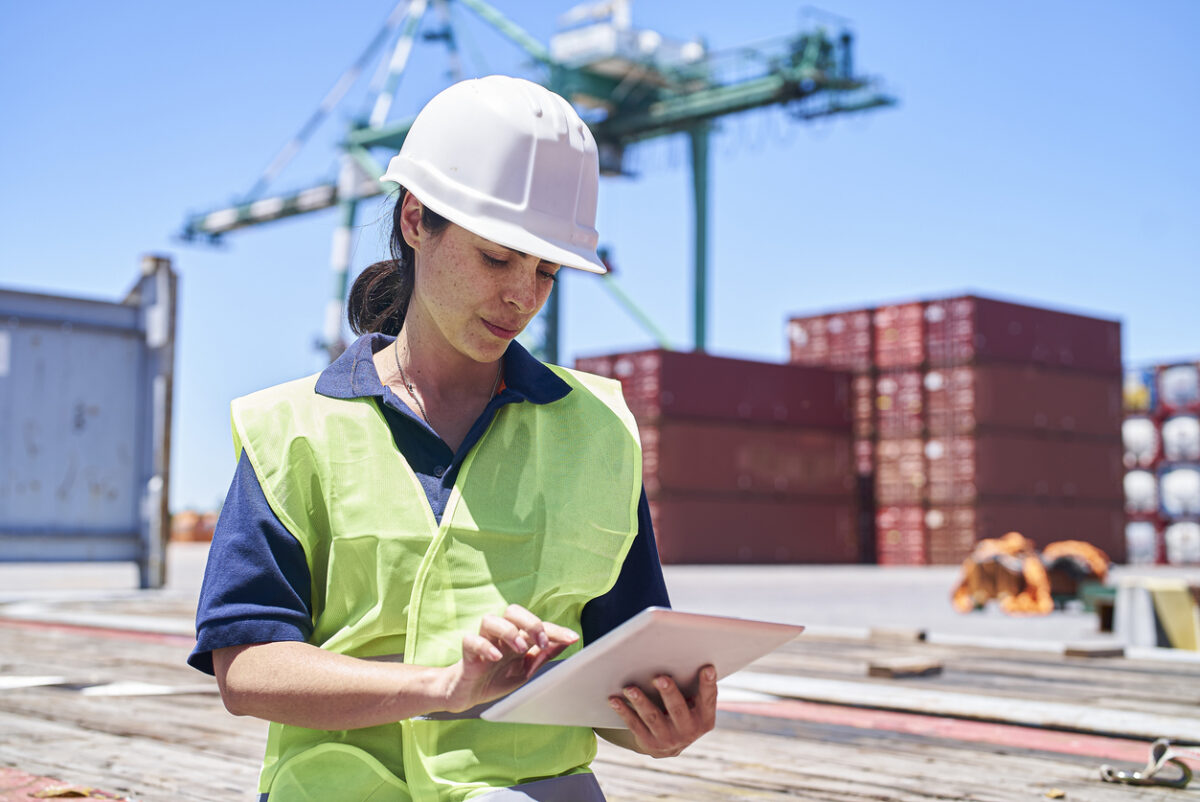 Female engineer sitting on ship dock while using digital tablet