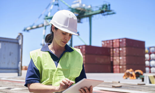 Female engineer sitting on ship dock while using digital tablet