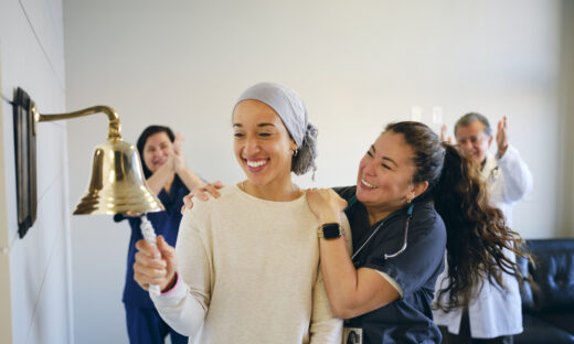 An adult woman chemotherapy patient in a treatment office, celebrating the completion of her treatment with a ceremonial bell ring. Actor portrayal