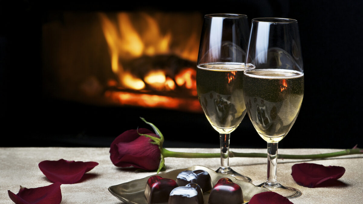 Two glasses of champagne, artisan chocolates and a rose by a cozy fire make for a romantic evening for two. Low key lighting; fire is reflected in glasses. Shallow DOF