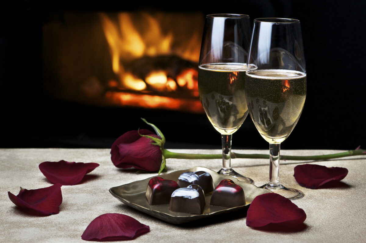 Two glasses of champagne, artisan chocolates and a rose by a cozy fire make for a romantic evening for two. Low key lighting; fire is reflected in glasses. Shallow DOF