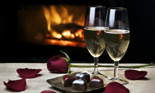 Two glasses of champagne, artisan chocolates and a rose by a cozy fire make for a romantic evening for two. Low key lighting; fire is reflected in glasses. Shallow DOF