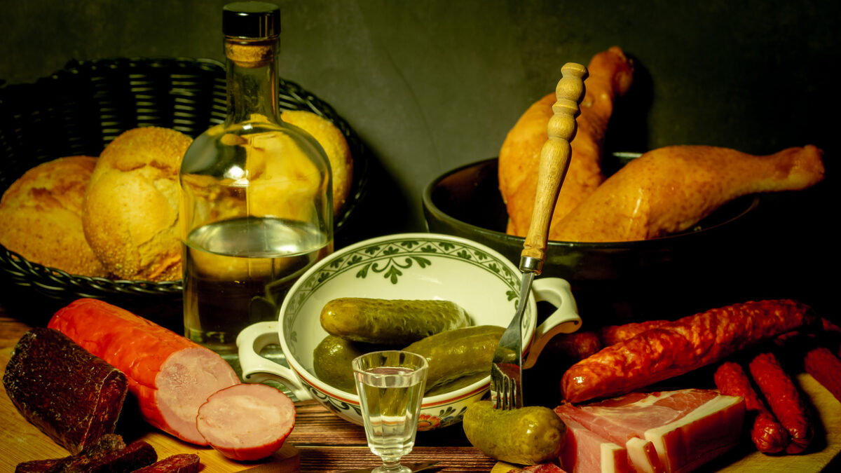 A stylized antique still life with meat, sausages, salami, lard and a glass of vodka