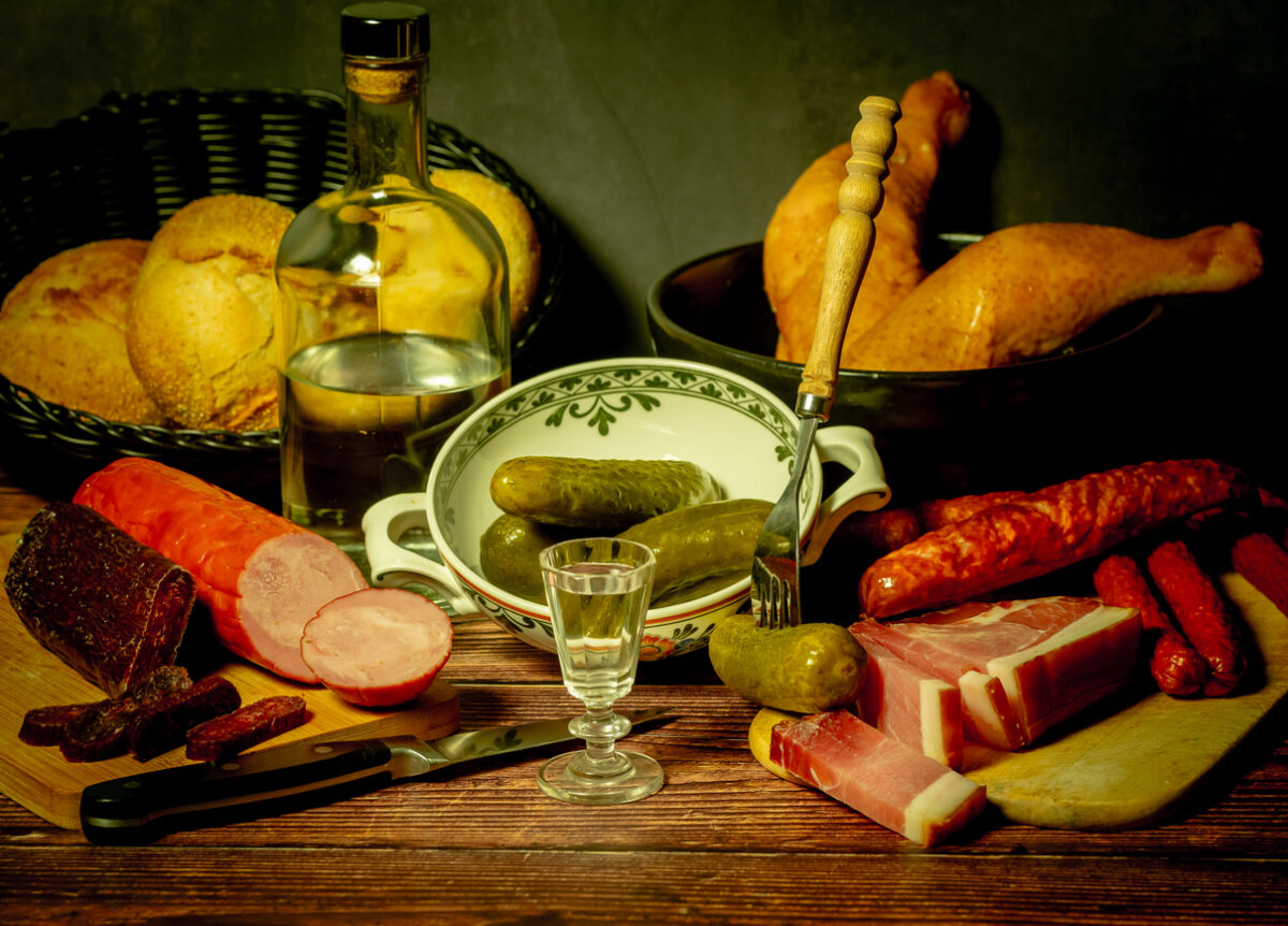 A stylized antique still life with meat, sausages, salami, lard and a glass of vodka