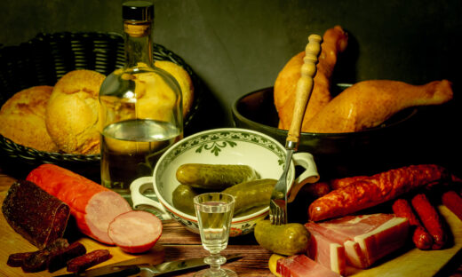 A stylized antique still life with meat, sausages, salami, lard and a glass of vodka