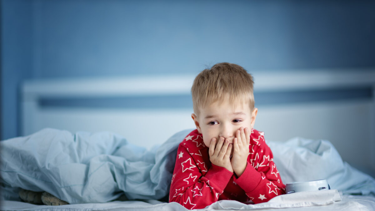 Sleepy boy lying in bed with blue beddings. Tired child in bedroom. Little kid lying awake in red pajamas with toothacheSleepy boy lying in bed with blue beddings. Tired child in bedroom sleeping. Little kid lying asleep in red pajamas with alarm clock