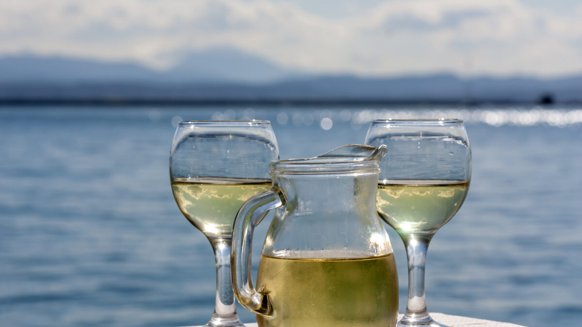 Two glasses and a jug of white wine in a rural tavern against the backdrop of the sea on a sunny spring day