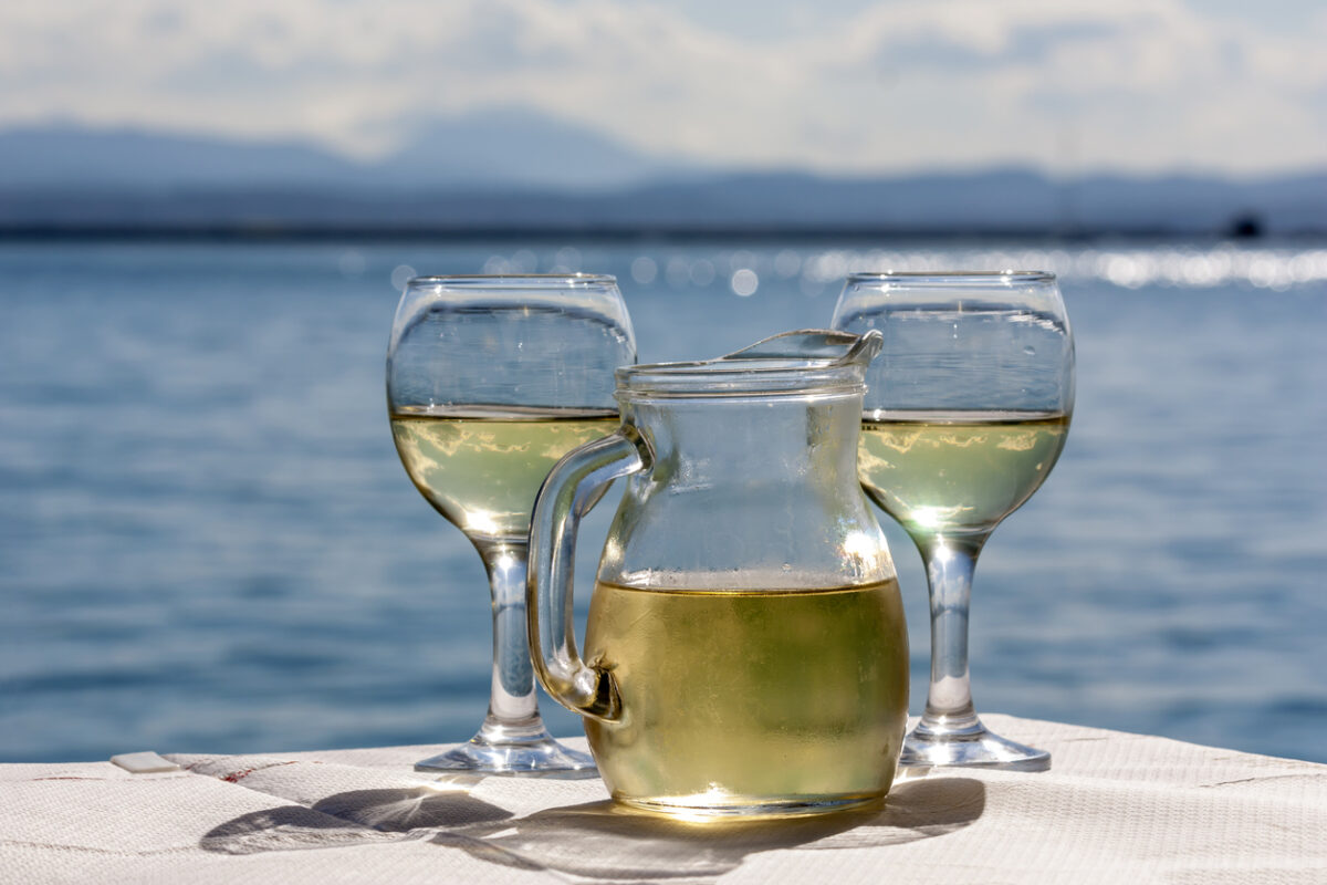 Two glasses and a jug of white wine in a rural tavern against the backdrop of the sea on a sunny spring day