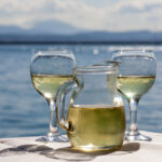 Two glasses and a jug of white wine in a rural tavern against the backdrop of the sea on a sunny spring day