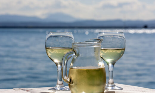 Two glasses and a jug of white wine in a rural tavern against the backdrop of the sea on a sunny spring day