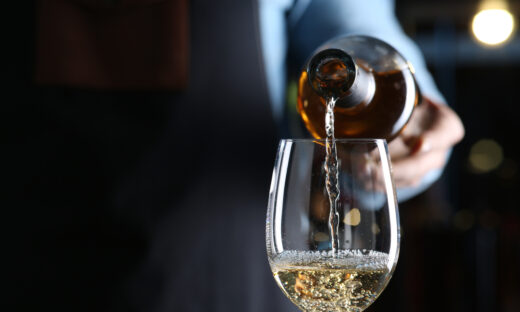 Bartender pouring white wine from bottle into glass indoors, closeup. Space for text