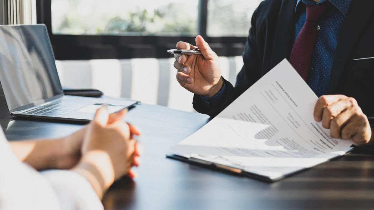 Businessman in suit in his office showing an insurance policy and pointing with a pen where the policyholder must to sign. Insurance agent presentation and consulting insurance detail to customer