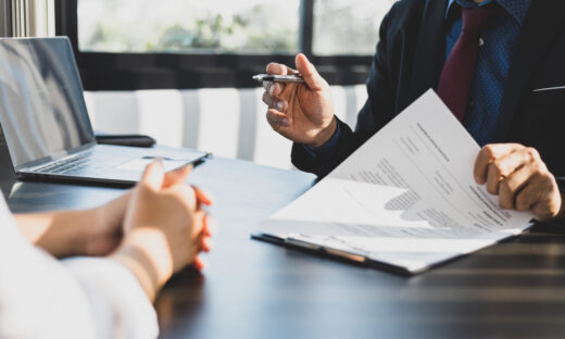 Businessman in suit in his office showing an insurance policy and pointing with a pen where the policyholder must to sign. Insurance agent presentation and consulting insurance detail to customer