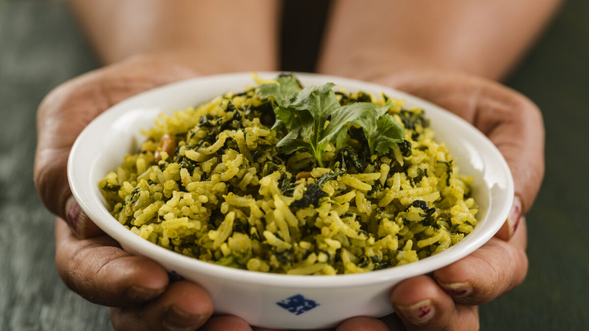 Hands holding bowl full of spinach rice and topped with cilantro