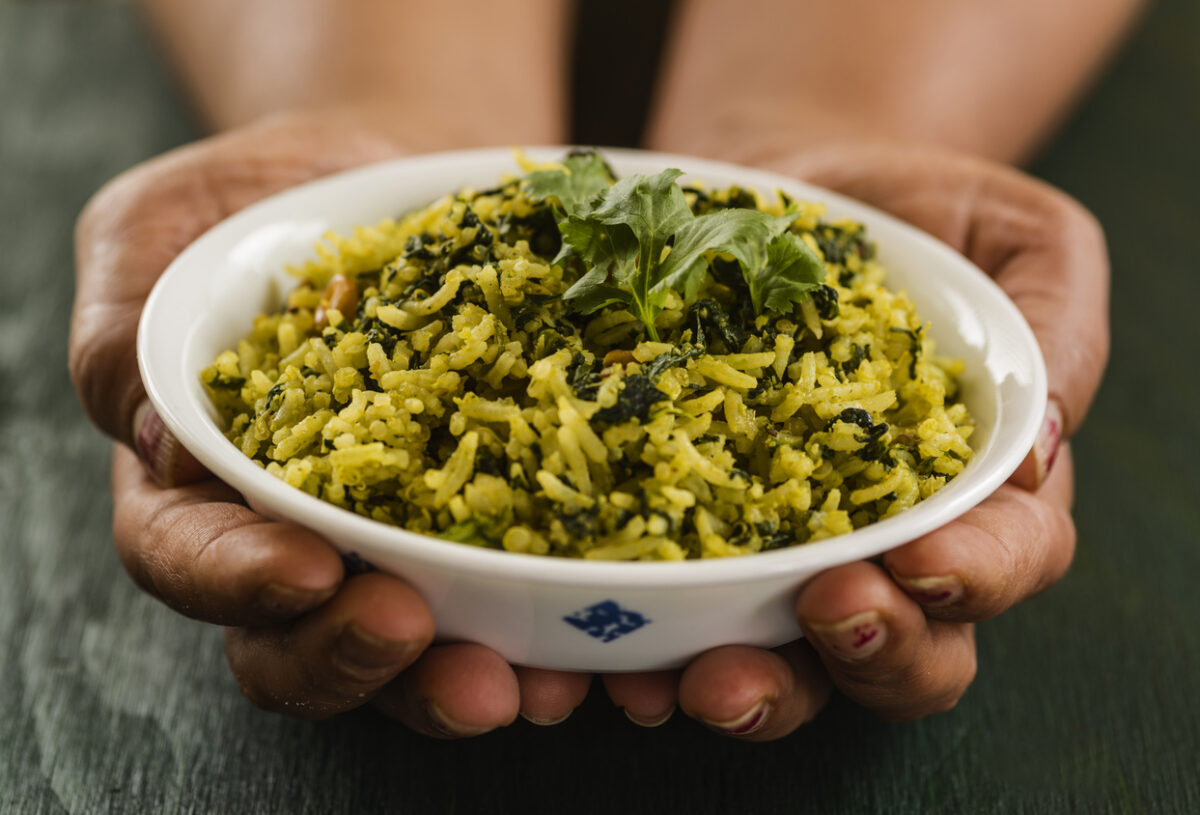 Hands holding bowl full of spinach rice and topped with cilantro