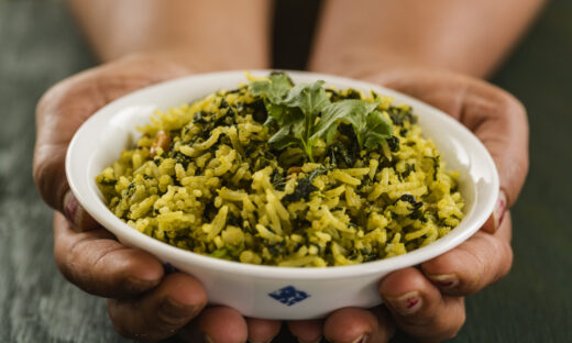 Hands holding bowl full of spinach rice and topped with cilantro